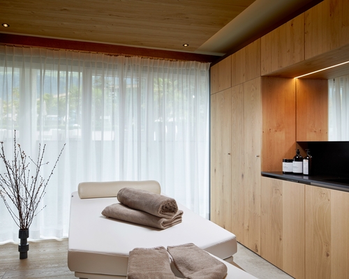 Un lettino wellness bianco con asciugamani piegati si trova davanti a tende chiare nella sala relax.