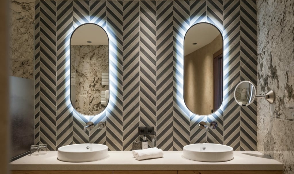 Doppelwaschtisch im Suite-Badezimmer Ein Doppelwaschtisch mit zwei ovalen Waschbecken und beleuchteten Spiegeln in einem stilvollen Badezimmer.