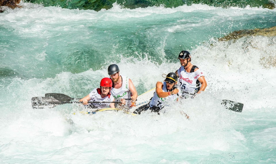 Quattro persone navigano su un gommone tra rapide spumeggianti durante una discesa di rafting.