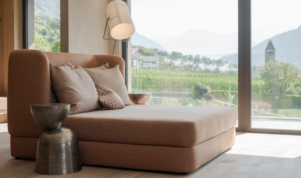 Una sala relax con chaise longue e vista sul paesaggio verde attraverso ampie finestre.