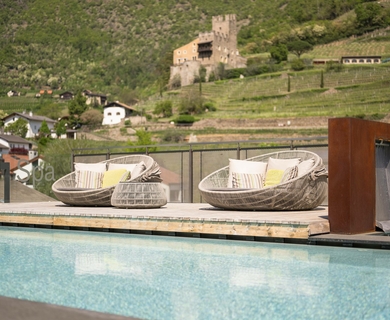 Poolterrasse mit Blick auf Schloss in Naturns Auf der Poolterrasse stehen zwei runde Loungesessel vor dem Becken, im Hintergrund liegen Weinberge und ein Schloss.