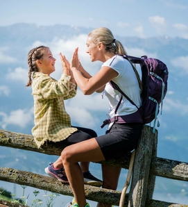 Eine Frau und ein Kind sitzen auf einem Holzzaun und geben sich in den Bergen High-Five.