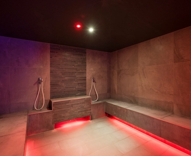 Sauna im Wellnesshotel Feldhof in Naturns Ein moderner Saunabereich mit Steinwänden, Holzelementen und roter Bodenbeleuchtung.