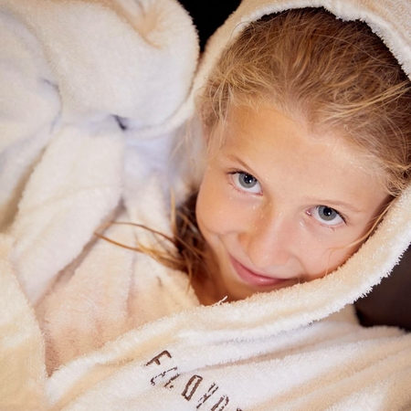 Child in bathrobe in the spa area A child lies in a soft hooded bathrobe and looks at the camera in a wellness area.
