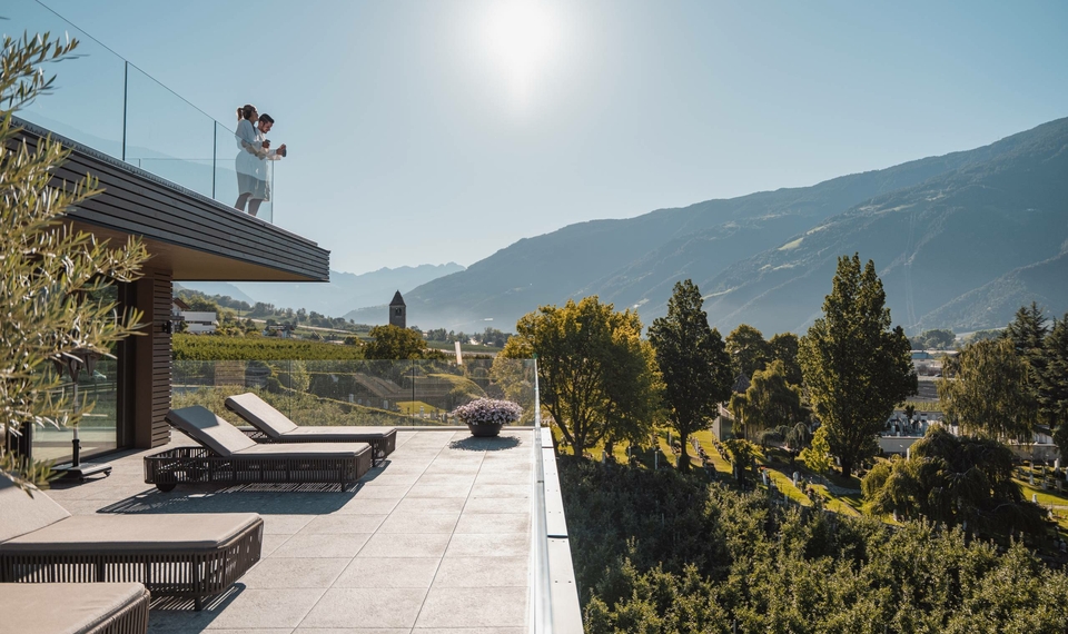 Eine Panoramaterrasse mit Liegen und Glasgeländer am Sky Spa, mit Blick auf Berge und Tal.