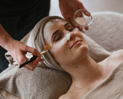 Eine Frau erhält eine Gesichtsbehandlung mit Creme im Wellnessbereich.