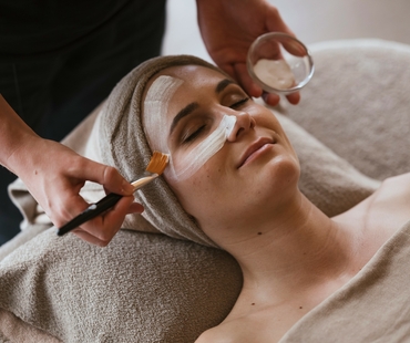 Eine Frau erhält eine Gesichtsbehandlung mit Creme im Wellnessbereich.