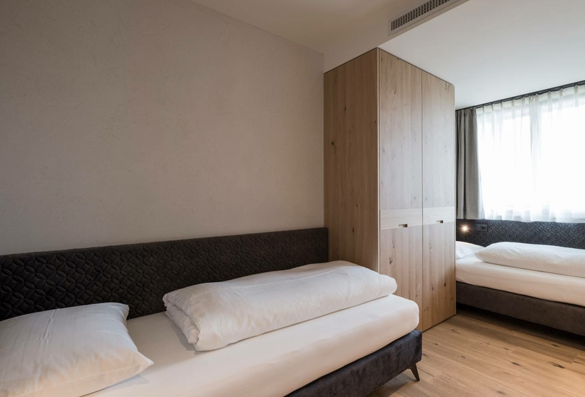 Suite Nature con letti singoli luminosi al Feldhof Una camera da letto semplice della Suite Nature con due letti singoli, armadio in legno e luce naturale.