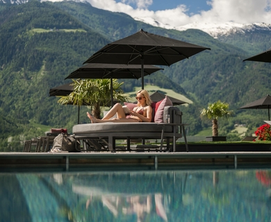 Pool-Liege mit Bergblick im Feldhof Resort Eine Frau entspannt auf einer Liege am Pool mit Blick auf die Berge.