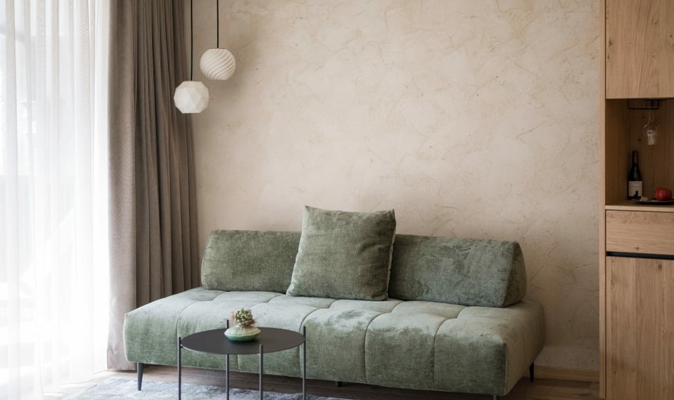Familiensuite im Feldhof mit grünem Sofa Ein grünes Sofa mit runden Tischen steht vor einer hellen Wand im modernen Wohnbereich der Suite.