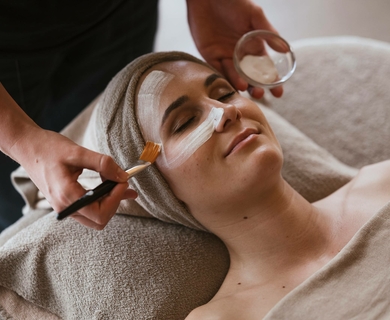 Gesichtsbehandlung im Wellnesshotel Feldhof Eine Frau erhält eine Gesichtsbehandlung mit Creme und Pinsel in einem ruhigen Spa-Bereich.