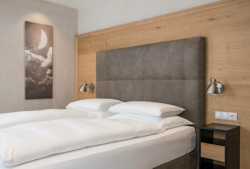 Un letto matrimoniale con testiera imbottita, boiserie in legno e decorazione murale essenziale nella camera.