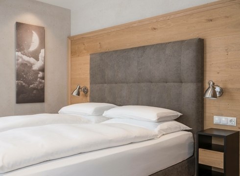 Un letto matrimoniale con testiera imbottita, boiserie in legno e decorazione murale essenziale nella camera.