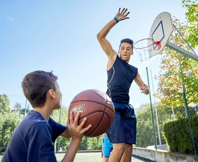 Jugendliche beim Basketball auf dem Outdoorplatz Zwei Jugendliche spielen Basketball auf einem Freiplatz, einer wirft zum Korb, der andere hält den Ball.