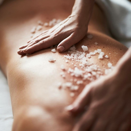 Wellnessbehandlung: Salzpeeling auf dem Rücken Hände tragen ein Salzpeeling auf den Rücken bei einer Wellnessbehandlung im Spa auf.