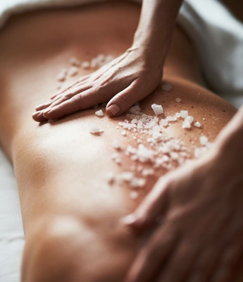 Wellnessbehandlung: Salzpeeling auf dem Rücken Hände tragen ein Salzpeeling auf den Rücken bei einer Wellnessbehandlung im Spa auf.