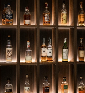 Mehrere Whiskyflaschen stehen in einem beleuchteten Holzregal an der Hotelbar.