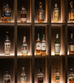 Mehrere Whiskyflaschen stehen in einem beleuchteten Holzregal an der Hotelbar.