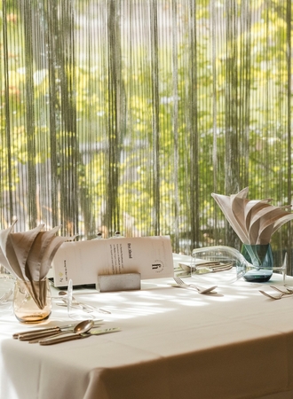 Ein gedeckter Tisch mit Menükarten und Besteck steht am Fenster im Hotelrestaurant.