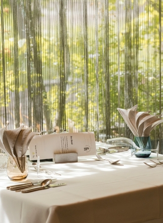 A set dining table with menus and cutlery stands by the window in the hotel restaurant.