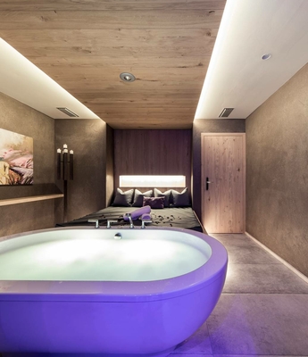 Wellnessbehandlung im Spa des Feldhof Eine violette Badewanne steht vor dem Bett in einem ruhigen Spa-Raum.