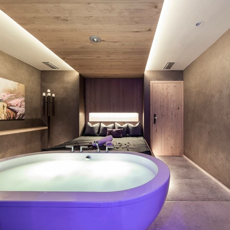 Wellnessbehandlung im Spa des Feldhof Eine violette Badewanne steht vor dem Bett in einem ruhigen Spa-Raum.