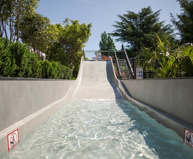 Poolrutsche im Feldhof DolceVita Resort Eine Poolrutsche mit flachem Wasserbecken führt zwischen grünen Pflanzen hinunter.