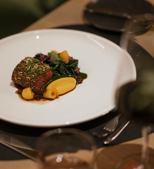 Ein fein angerichtetes Fleischgericht mit Gemüse auf einem weißen Teller in einem eleganten Hotelrestaurant.