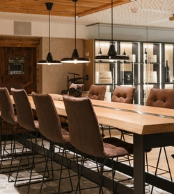 Ein langer Holztisch mit Barhockern steht vor einer beleuchteten Weintheke im Hotelrestaurant.