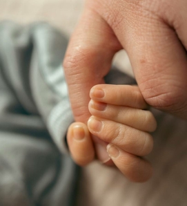 Ein Baby hält einen erwachsenen Finger in einer nahen Aufnahme.
