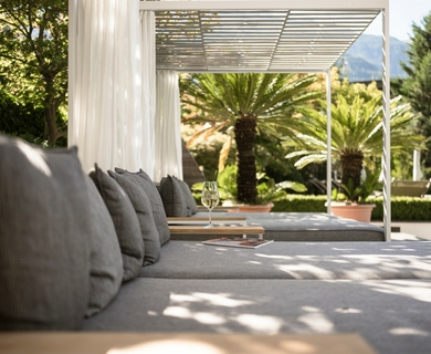 Ruhelounge im Wellnesshotel in Naturns Eine ruhige Liegefläche mit grauen Kissen unter einer Pergola im Garten des Resorts.