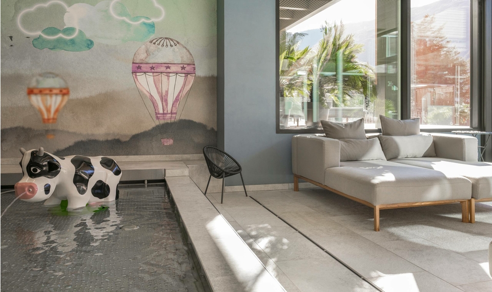 Ein heller Ruhebereich mit Sofa, Kinder-Sitzmöbeln und einem flachen Wasserbecken an der Wand.