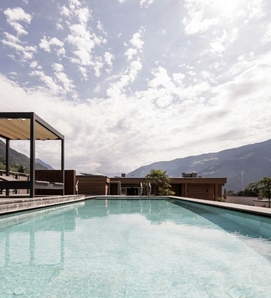 Ein rechteckiger Infinity-Pool mit Blick auf die Berge unter einem hellen, wolkigen Himmel.