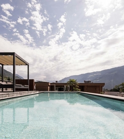 Ein rechteckiger Infinity-Pool mit Blick auf die Berge unter einem hellen, wolkigen Himmel.