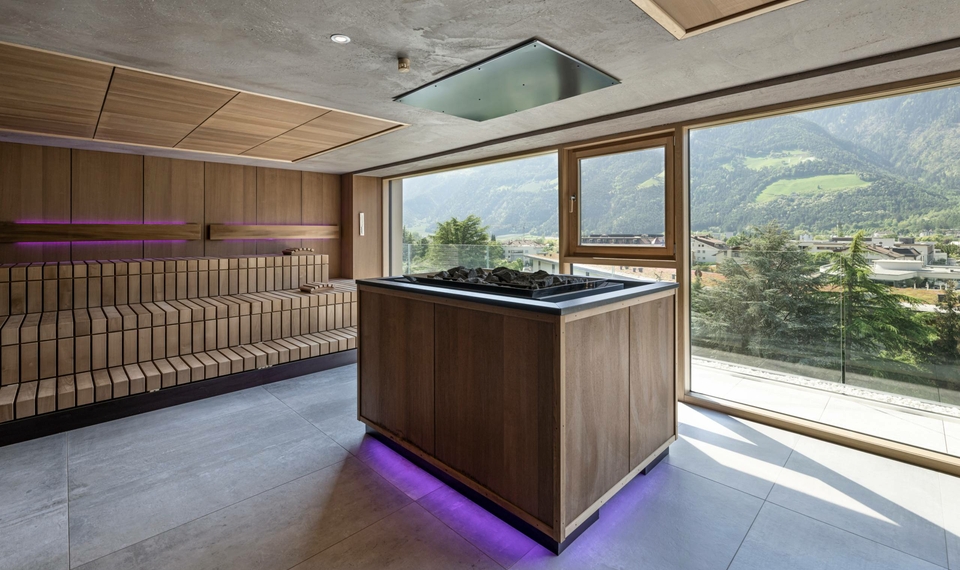 Eine moderne Sauna mit Holzvertäfelung und Blick durch große Fenster auf die Berge.