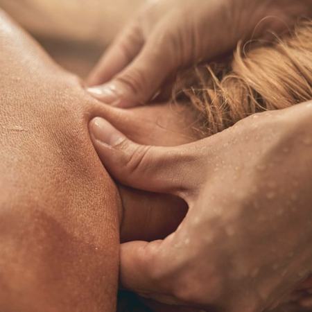 Le mani massaggiano il collo di una persona durante un trattamento benessere nella spa.