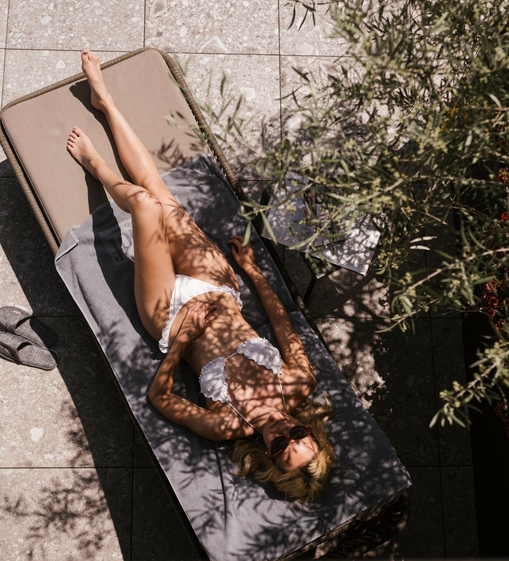 Eine Frau liegt entspannt auf einer Liege im Adults Only Spa, teilweise von Pflanzenschatten bedeckt.