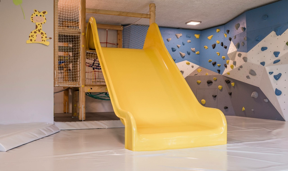 Eine gelbe Rutsche steht in einem gepolsterten Kinderbereich mit Kletterwand im Familienhotel.