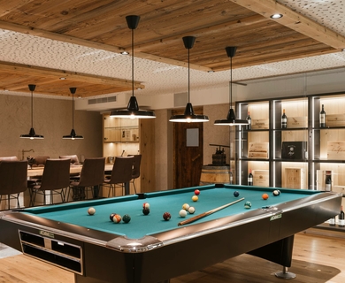 Billardraum im Feldhof DolceVita Resort Ein Billardtisch steht in einem hellen Aufenthaltsraum mit Barhockern und Regalen.
