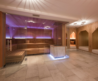 Family Sauna im Feldhof DolceVita Resort Ein großzügiger Saunabereich mit Holzliegen, Glasfront und gedämpfter Beleuchtung.