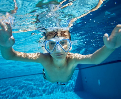 Familienurlaub im Pool mit Schnorchelkind Ein Kind mit Schnorchelmaske taucht im Pool unter Wasser und hält die Hände ausgestreckt nach vorn.