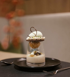 Ein feines Dessert im Glas auf einem Teller im Hotelrestaurant, mit Creme, Dekor und Schokoladenelementen.