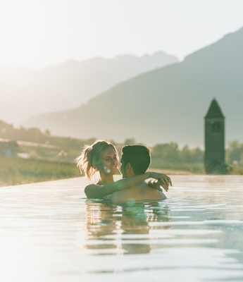 A couple stands in an infinity pool with mountain views in the warm light of the evening sun.