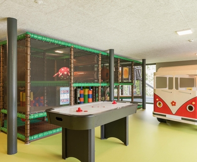 Kinder- und Jugendbereich mit Airhockey im Feldhof Ein Airhockey-Tisch steht vor einem abgetrennten Spielbereich mit Kletterelementen und einem Spielbus.